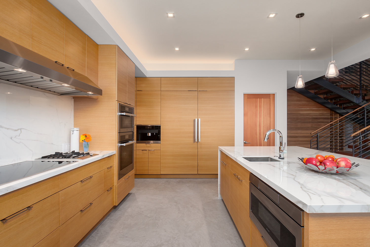 contemporary kitchen with marble countertops and wood cupboards and a bowl of red apples on the counter
