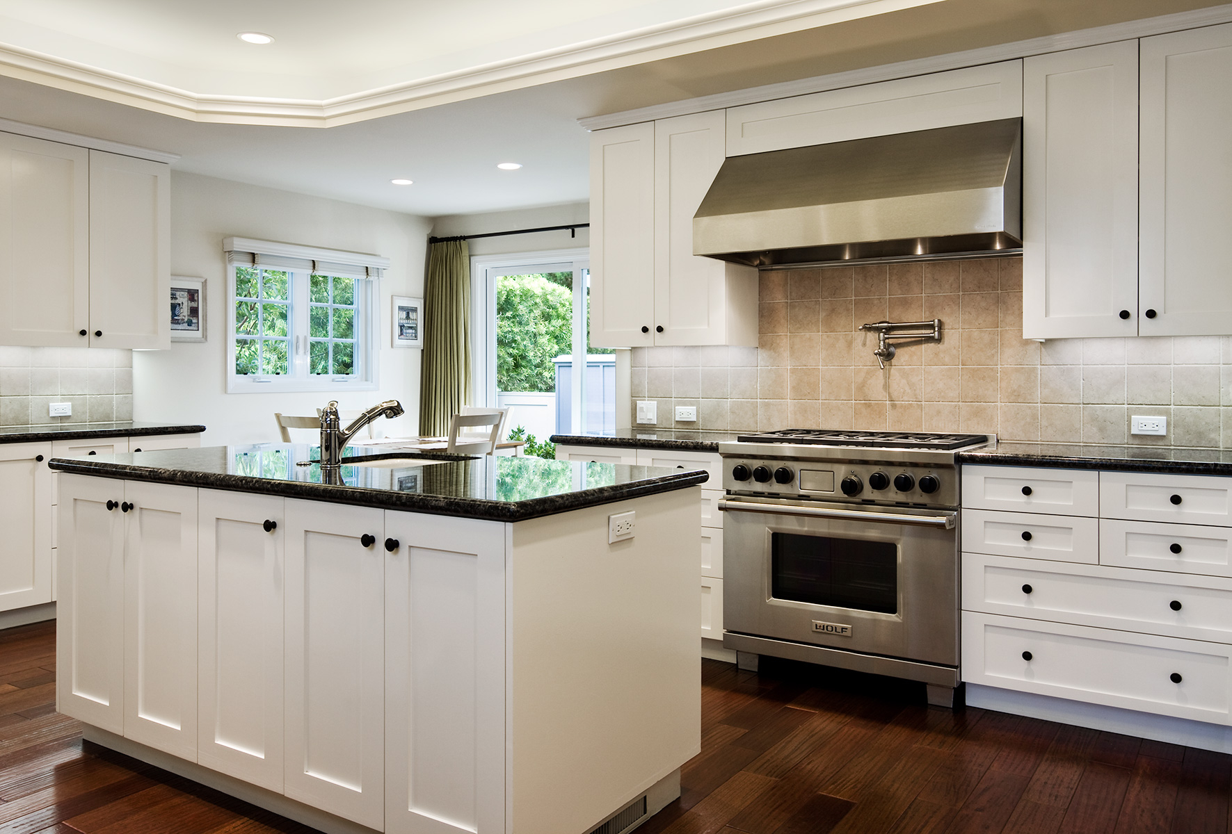 traditional kitchen with wood floors and white cabinets and dark marble countertops